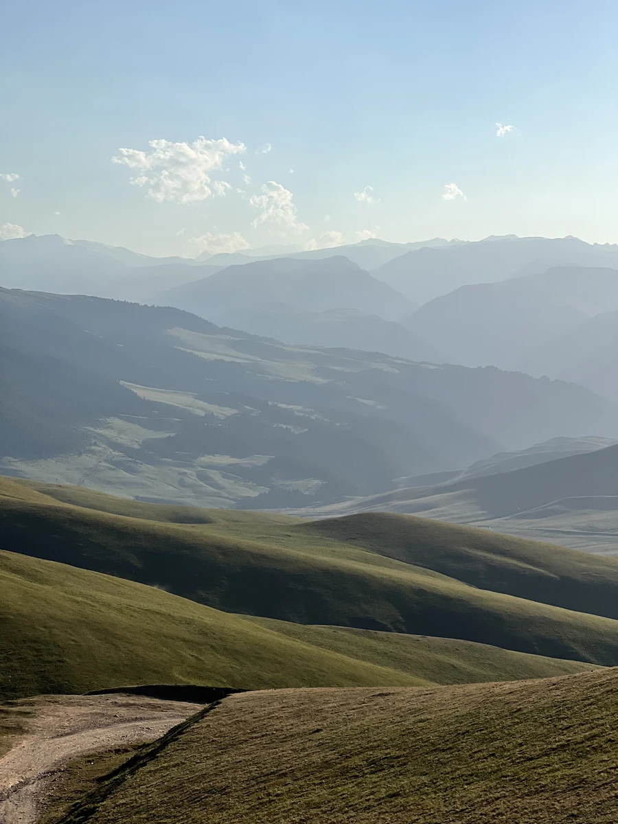 Dirt road winding across the rolling green hills of the Assy Plateau highlands